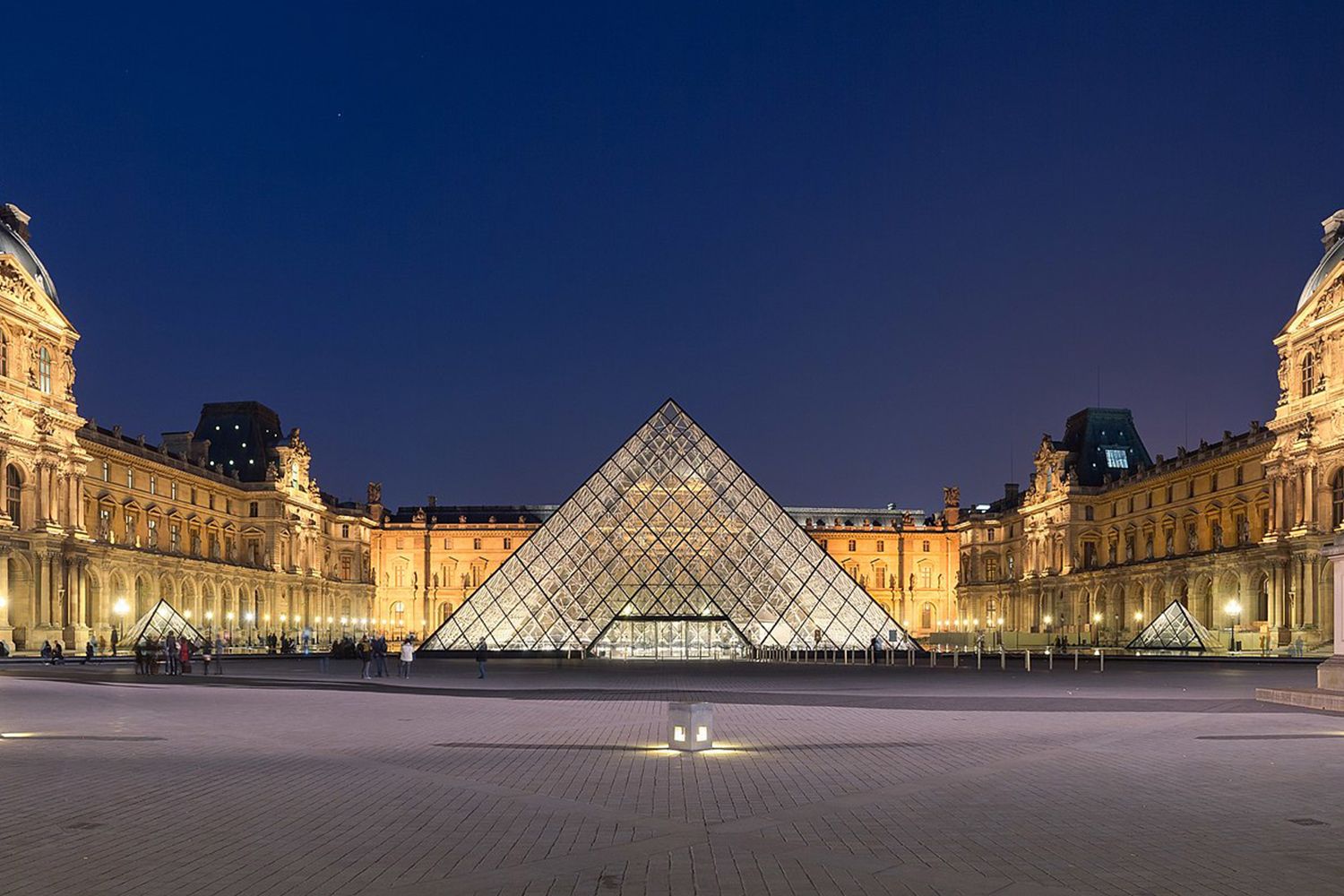 La pyramide du Louvre illuminée au crépuscule, reflet sur la cour Napoléon.
