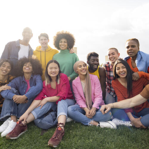 Un grand groupe de jeunes amis multiraciaux assis sur l'herbe, s'enlaçant et souriant au soleil.