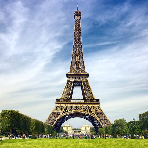 Vue de la tour Eiffel depuis le sol, entourée d’une allée verte et d’arbres.