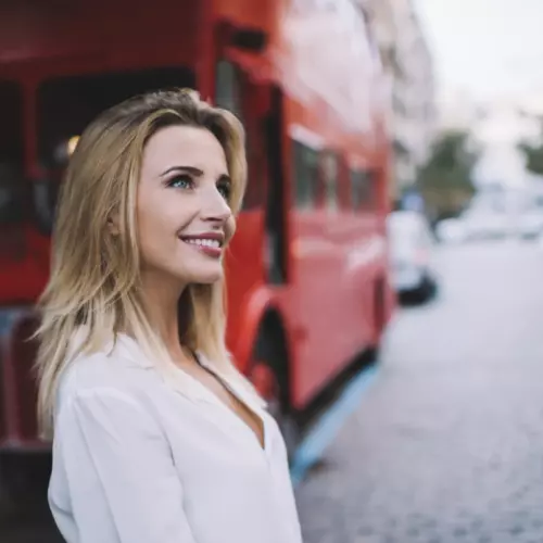Une fille au premier plan avec un bus touristique à deux étages et un touriste en arrière-plan.