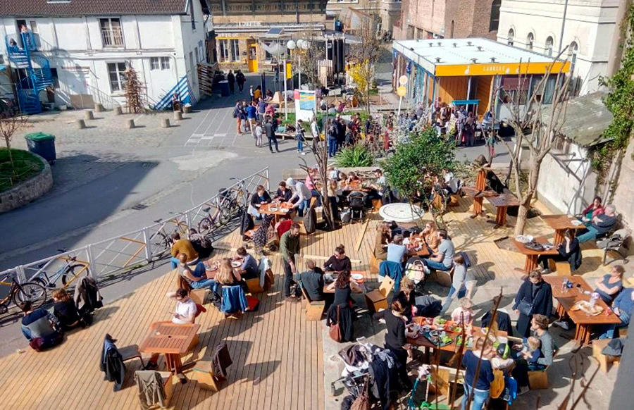 Vue du Jardin des Grands Voisins avec des personnes profitant d’un repas en plein air.